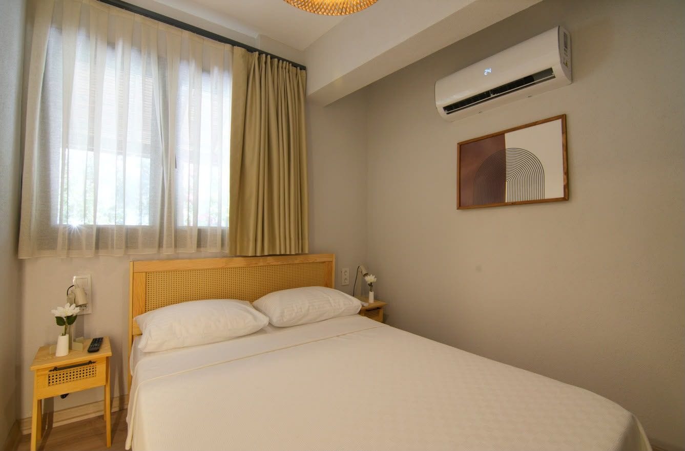 Une chambre d’hôtel avec un lit, une table de chevet, un climatiseur fixé au mur et une fenêtre avec des rideaux.