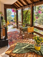 A wooden deck with a table and chairs, a potted lemon tree, and a view of the sea through large windows.