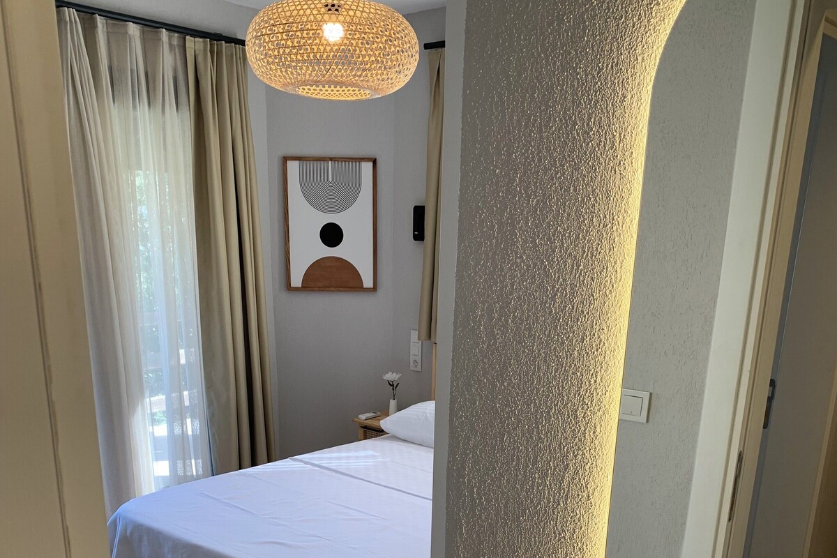 Une chambre à coucher avec un lit, un luminaire suspendu, une œuvre d’art encadrée et un miroir au mur.