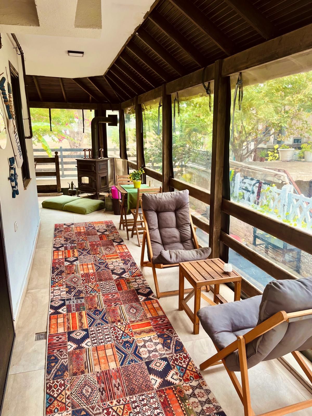 Un espacio de estar al aire libre cubierto con alfombra estampada, muebles de madera y vistas al verdor.