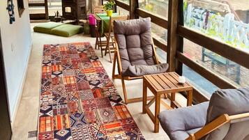 Un espacio de estar al aire libre cubierto con alfombra estampada, muebles de madera y vistas al verdor.
