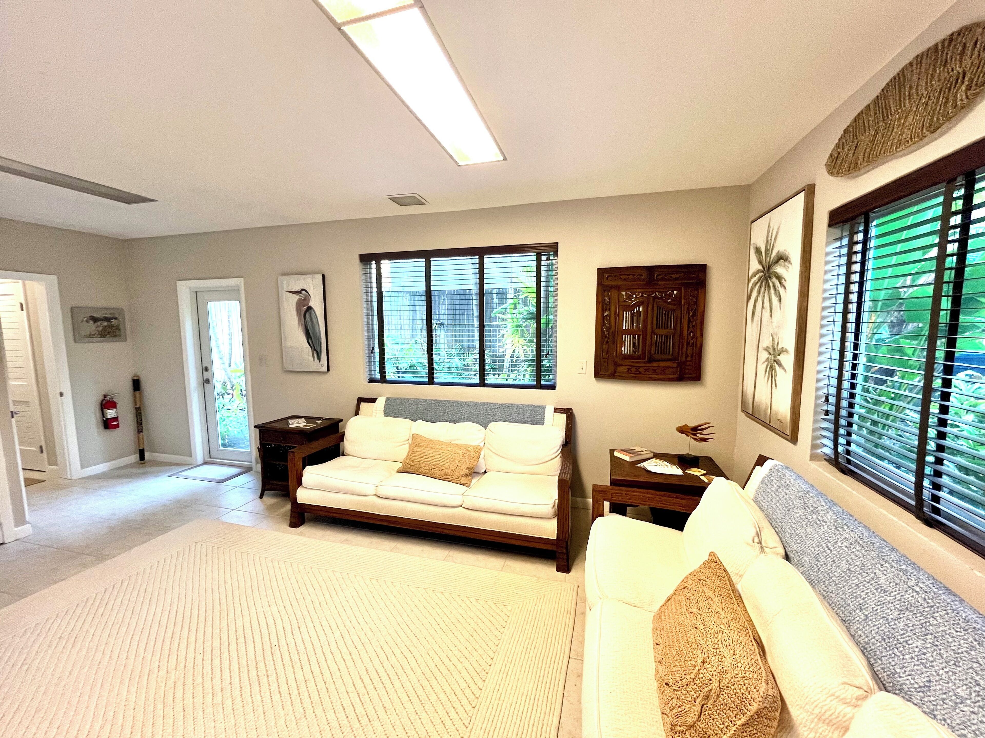 A well-lit living room with a sofa, a coffee table, and a fireplace. There is a window with blinds, a door, and a framed picture on the wall.