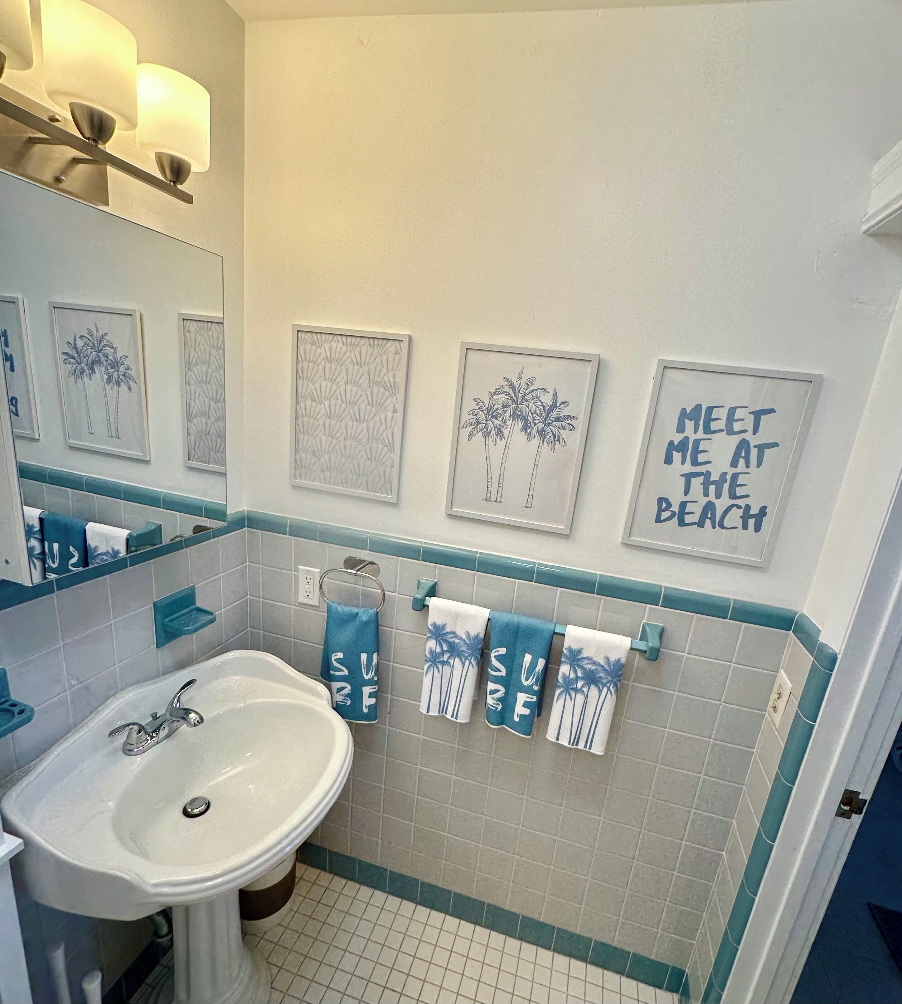 Baño con lavamanos, espejo y toallero con toallas de temática playera.