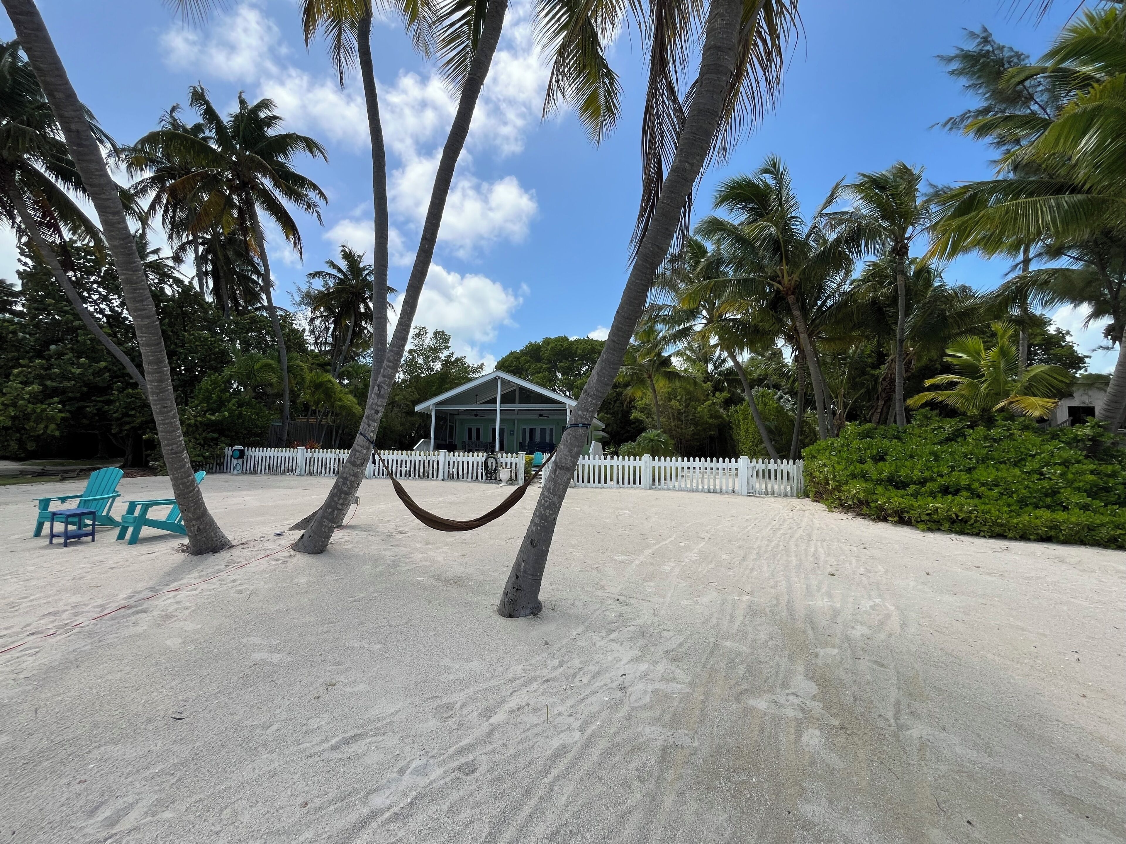 A beach with a white picket fence, a hammock, and turquoise chairs.