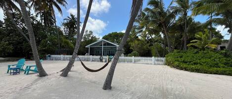 A beach with a white picket fence, a hammock, and turquoise chairs.