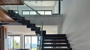 A modern interior with a glass staircase, a black sofa, and a view of the outdoors. - Casa Marlin (Jaco)
