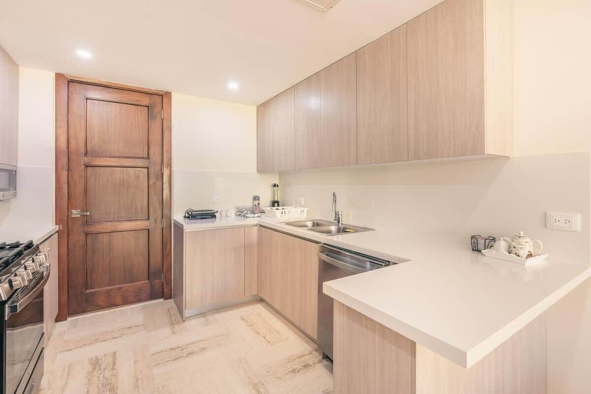 Una cocina moderna con armarios de madera, encimera blanca, lavavajillas integrado y estufa.