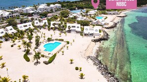 Una casa de playa con piscina, edificios blancos y una vista despejada del océano.