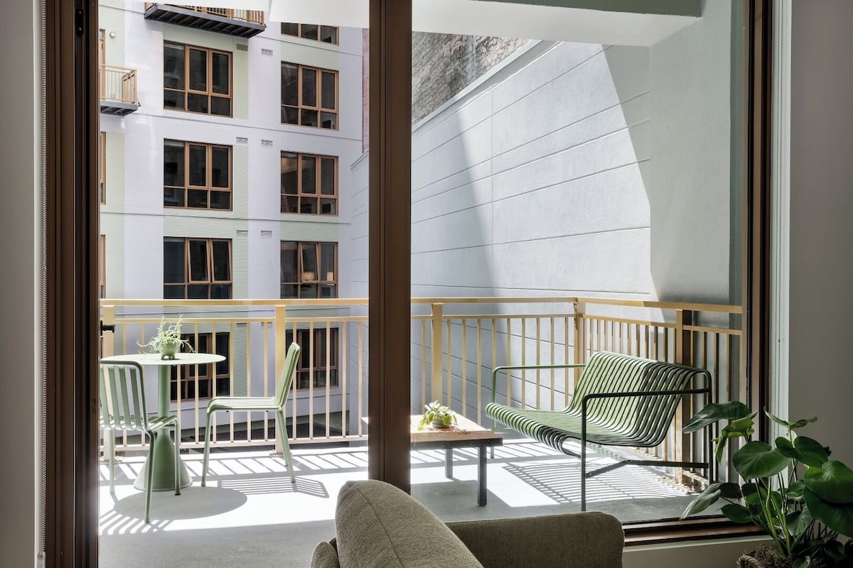 A balcony with a sofa, chairs, and a small table, overlooking a building with multiple windows.