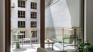 A balcony with a sofa, chairs, and a small table, overlooking a building with multiple windows.