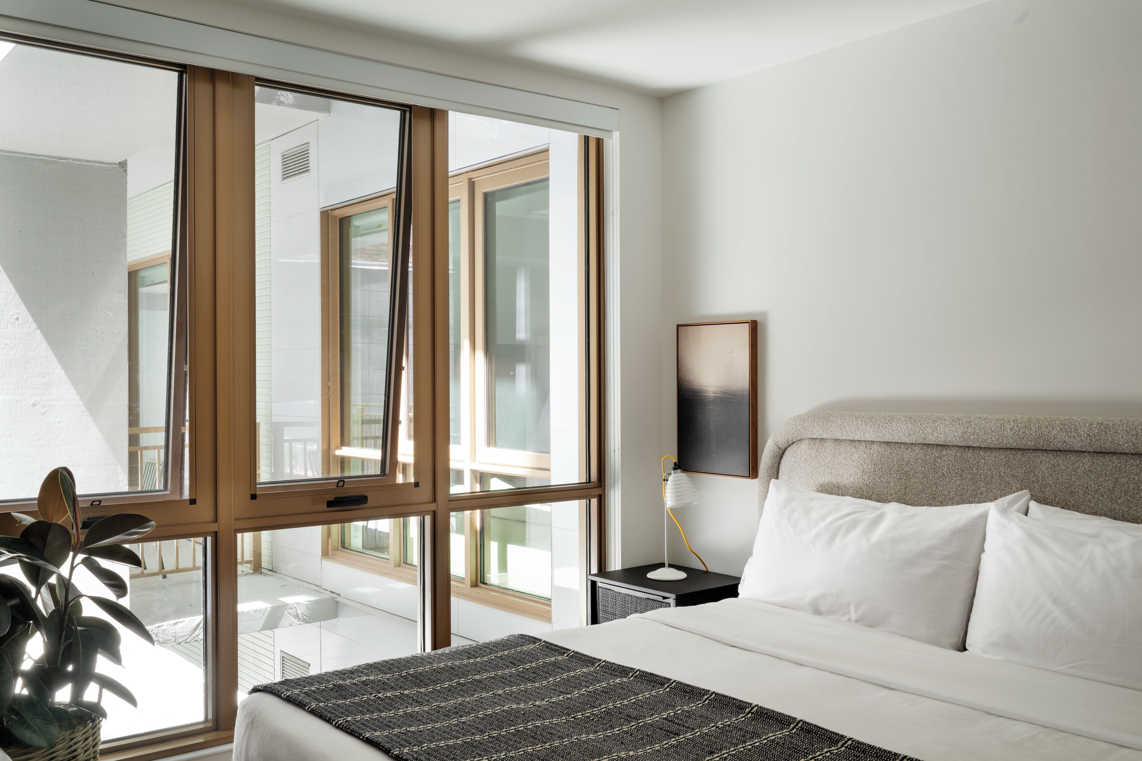 A hotel room with a bed, bedside lamp, and a view through a large window.