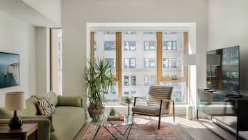 A modern living room with a sofa, a glass coffee table, a chair, a TV, and a large window with a city view.