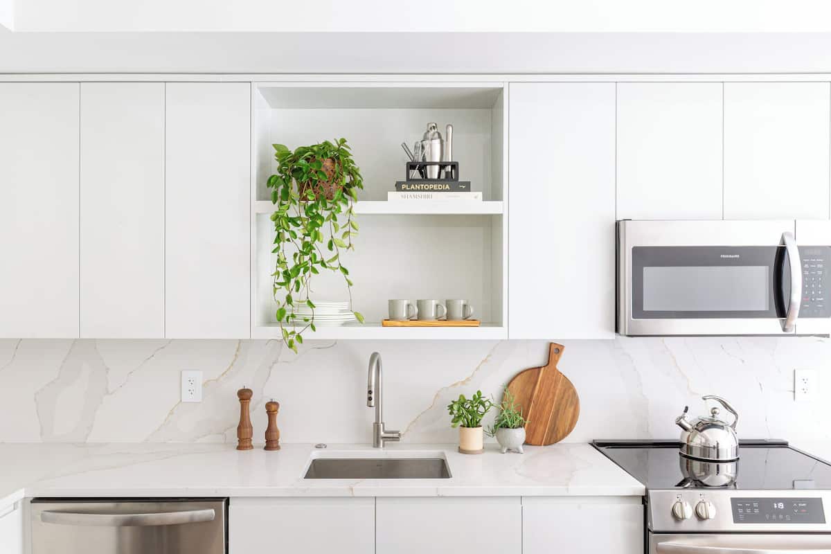 A modern kitchen with white cabinetry, a built-in microwave, a stainless steel sink, and a stove.