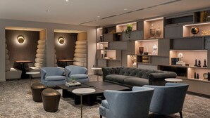 A modern living room with a grey sofa, blue armchairs, and a coffee table. There are shelves with decorative items and a plant.