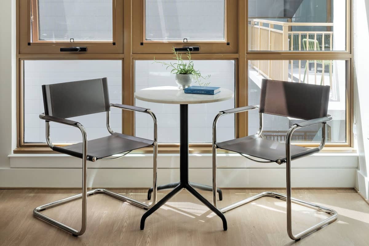 A modern room with a large window, two chairs, a small table, and a potted plant.
