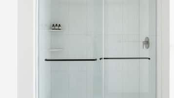 A glass-enclosed shower with a black handle and a shelf with toiletries.