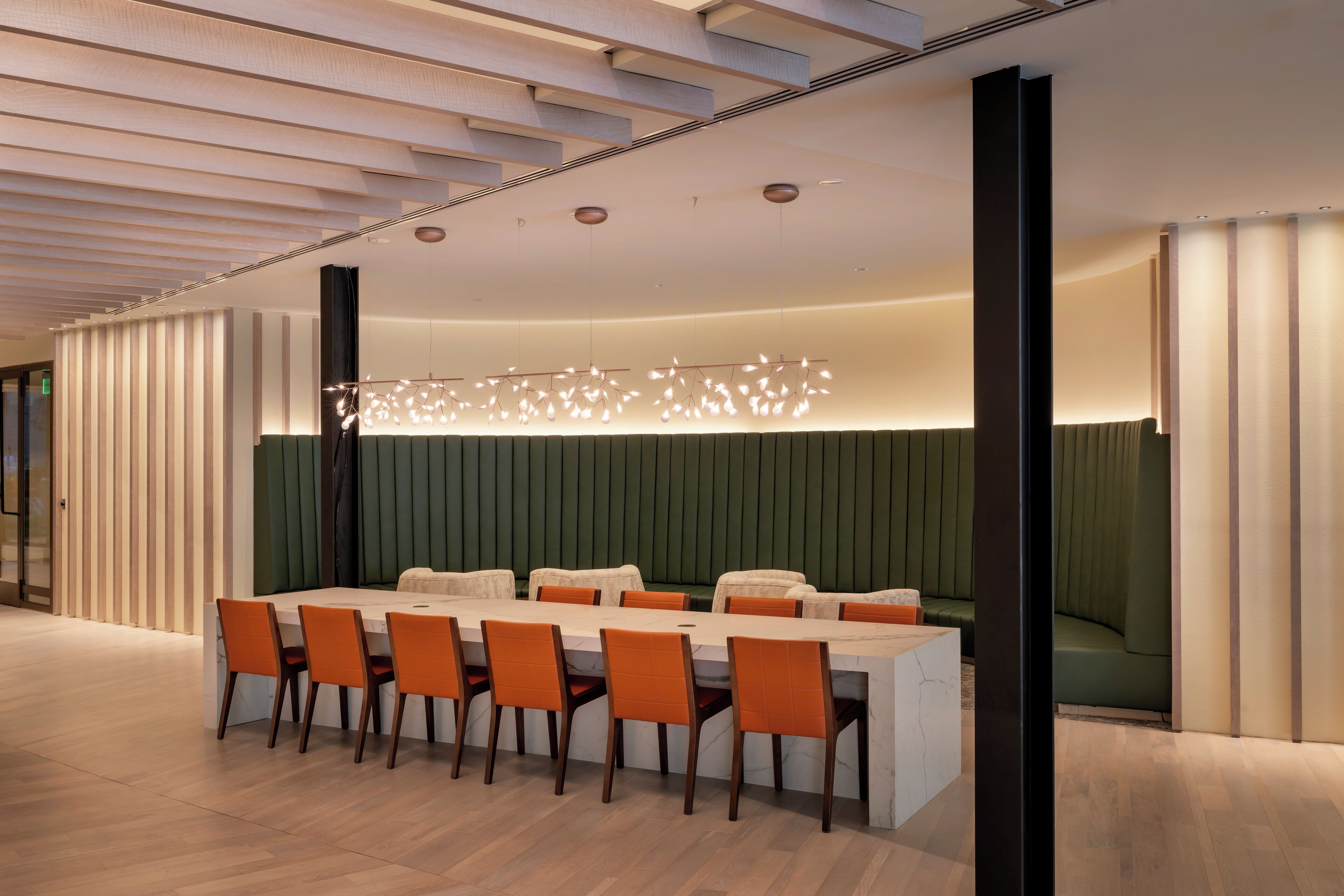 A modern dining area with a long table, orange chairs, and a unique ceiling light fixture.