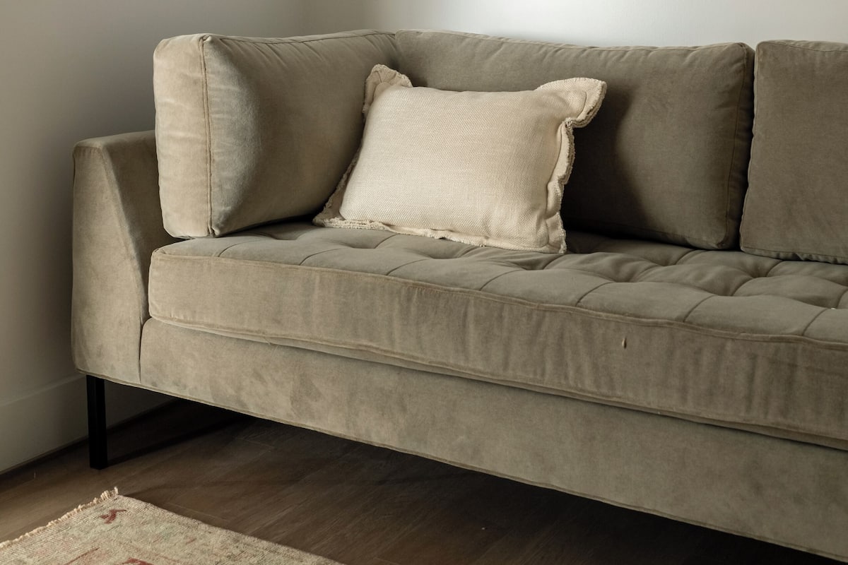 A neutral-toned sofa with a cushion, positioned against a plain wall with a framed artwork above it.