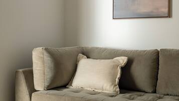 A neutral-toned sofa with a cushion, positioned against a plain wall with a framed artwork above it.