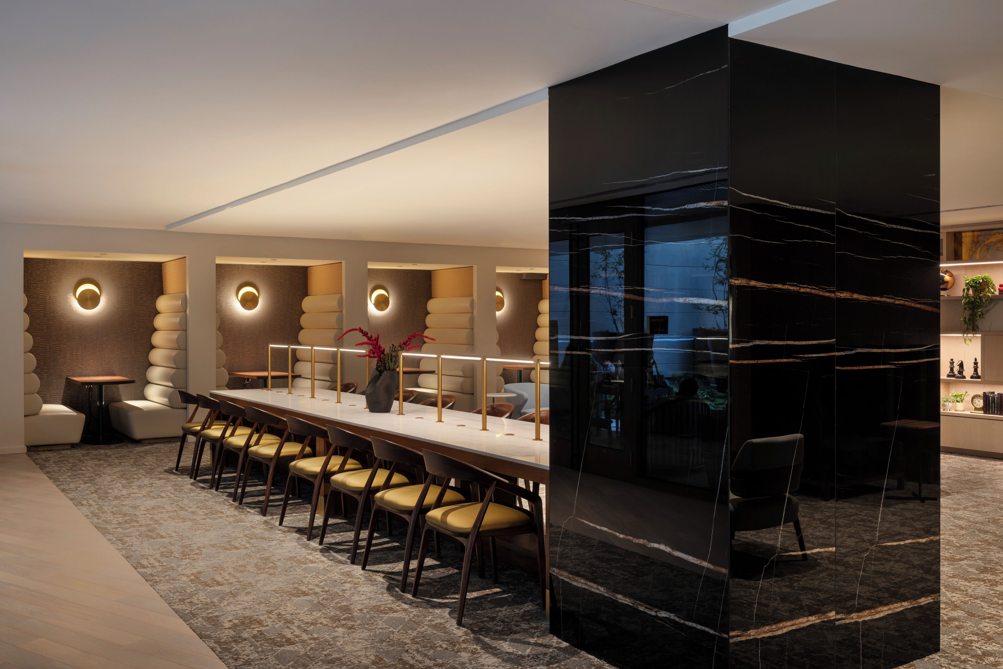 A modern dining area with a long table, multiple chairs, and a black accent wall with a circular design.