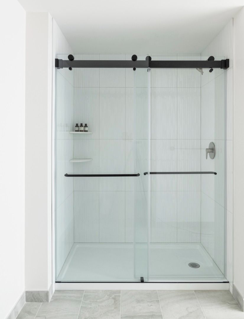 A glass-enclosed shower with a black handle and a shelf with toiletries.