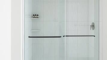 A glass-enclosed shower with a black handle and a shelf with toiletries.