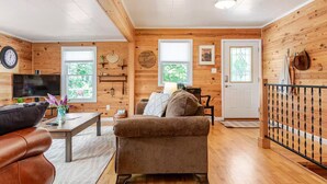 En mysig stuga med träpanel på väggarna, en soffa, en tv och en matplats.