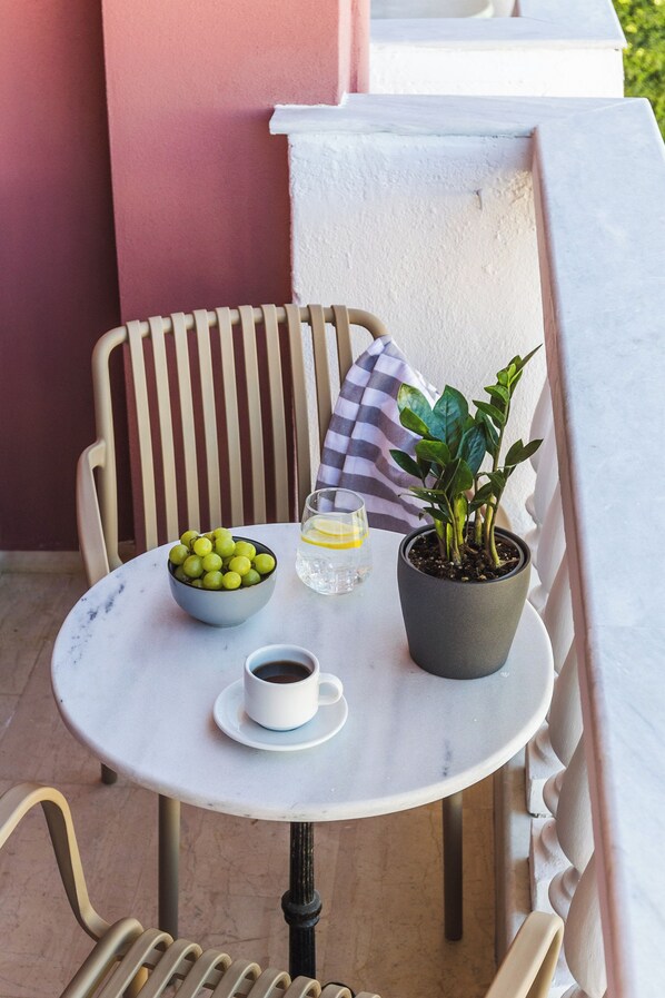 A small round table with a white marble top, a bowl of green grapes, a potted plant, a glass of water, and a cup of coffee.