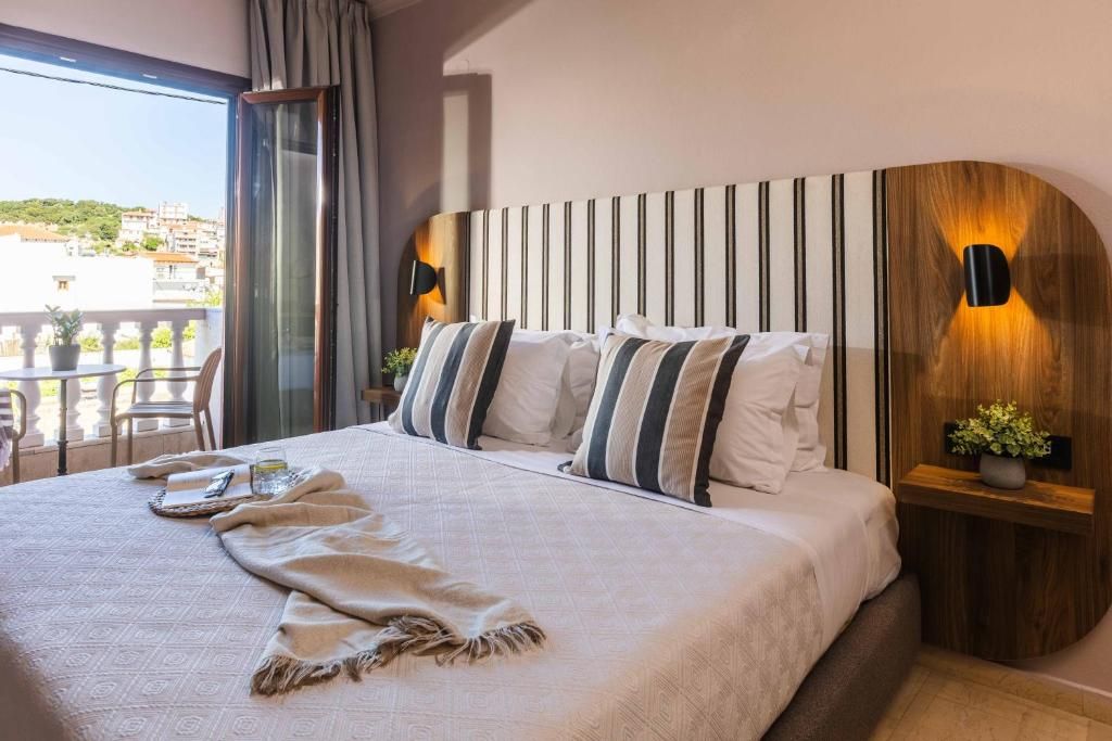 Habitación de hotel con una cama grande, vistas a la ciudad y un balcón con mobiliario exterior.