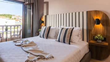 Habitación de hotel con una cama grande, vistas a la ciudad y un balcón con mobiliario exterior.