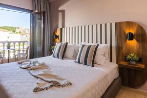 Habitación de hotel con una cama grande, vistas a la ciudad y un balcón con mobiliario exterior.