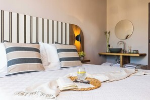 Een netjes opgemaakt bed met gestreepte kussens, een nachtkastje met een schaal en een spiegel, en een plantje op het nachtkastje.
