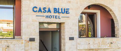 Un hotel llamado "Casa Blue" con fachada de piedra, un balcón con barandilla blanca y una entrada visible.