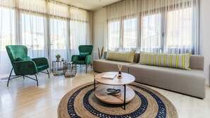 A modern living room with a sofa, two green armchairs, a round coffee table, and a patterned rug. - Casa Blue Hotel (Skiathos)