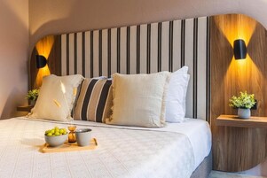 Una cama bien hecha con cabecera a rayas, mesitas de noche con lámparas y una pequeña planta en un estante.