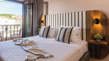 A hotel room with a large bed, a view of the city, and a balcony with outdoor seating.
