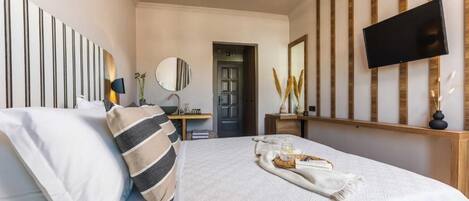 Une chambre à coucher comprenant un lit, un téléviseur à écran plat fixé au mur, une table de chevet avec une lampe et une porte donnant sur une autre pièce.