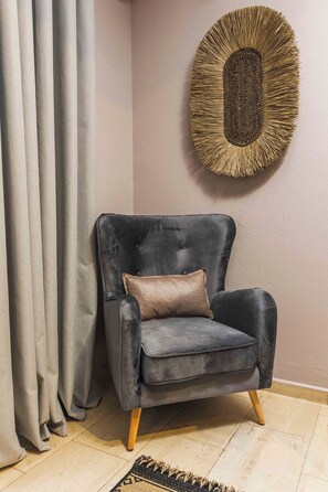 A dark grey armchair with wooden legs, a brown cushion, and a woven wall art piece above it. - Casa Blue Hotel (Skiathos)