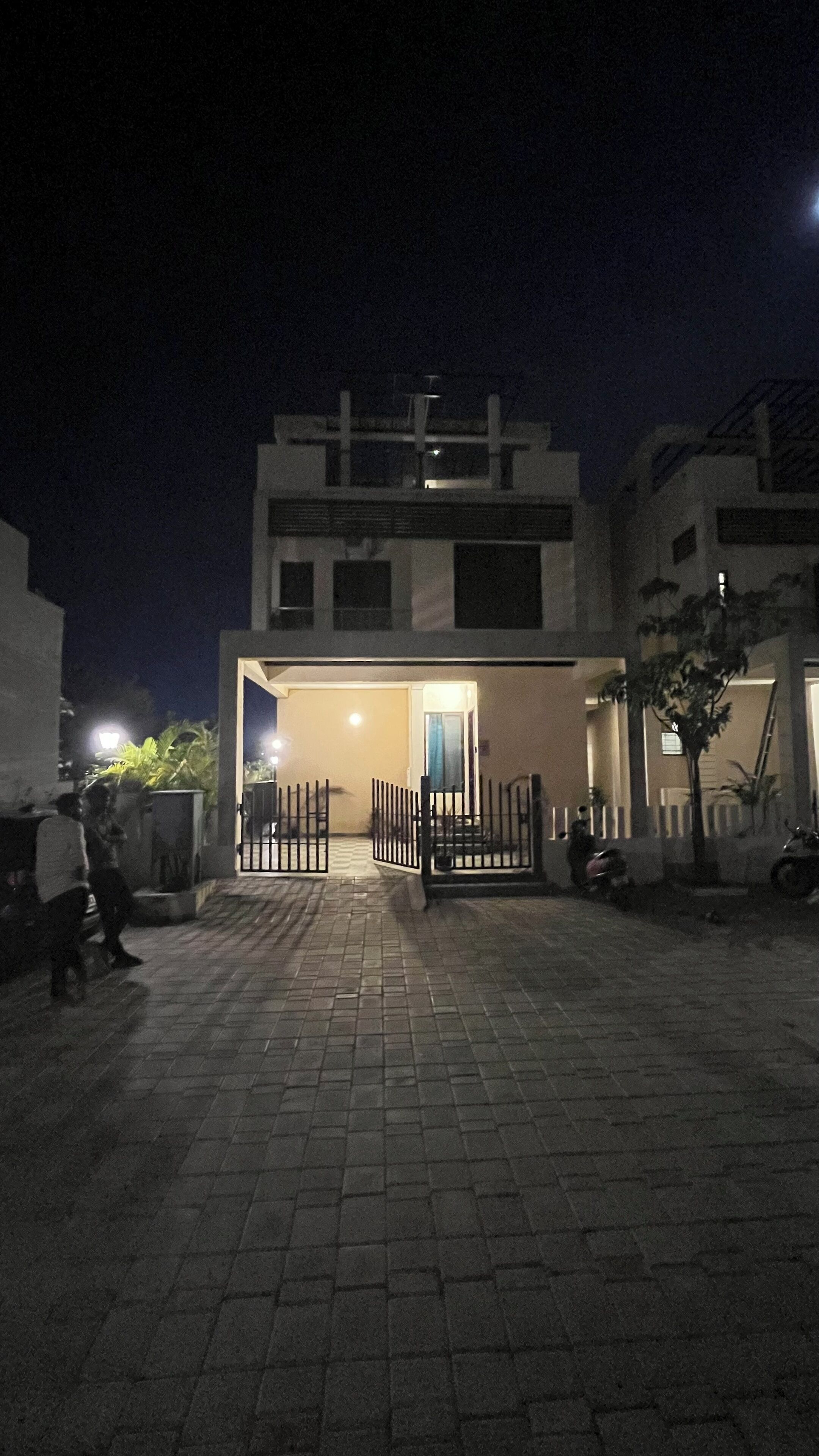 A modern building with a gated entrance, paved driveway, and a well-lit interior.