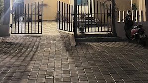 A modern two-story building with a gated entrance, a covered driveway, and a parked scooter. - Velvet vista (Tirupporur)