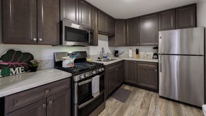 A modern kitchen with dark wood cabinets, stainless steel appliances, and a marble countertop.