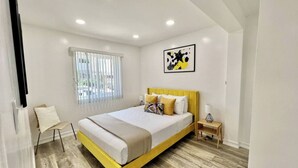 A modern bedroom with a bed, bedside table, and a window with blinds.