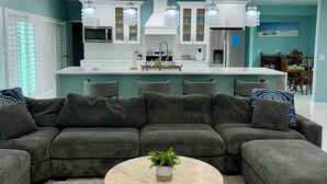 Una sala de estar moderna con un sofá modular, una mesa de centro redonda y una cocina al fondo.
