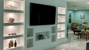 Una sala de estar moderna con un televisor de pantalla plana montado en la pared, rodeada de estanterías con objetos decorativos.