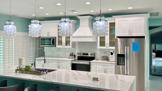 Una cocina moderna con una isla grande, armarios blancos, electrodomésticos de acero inoxidable e iluminación colgante.