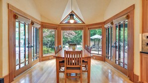 Un comedor amplio con una gran mesa de madera y sillas, rodeado de ventanas que dan a un jardín.