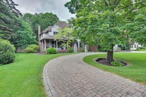 A brick pathway leading to a house with a stone chimney, surrounded by lush greenery and trees. - Hot Tub, Gym, Game Room! Luxe Estate in Longmeadow (Longmeadow)