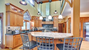 Una cocina amplia con gabinetes de madera, una isla de granito e iluminación colgante.