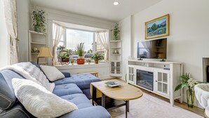 A living room with a blue sofa, a wooden coffee table, a television on a white cabinet, and various plants. - Walk to Beach & Shops: Dtwn Anacortes Apartment! (Anacortes)