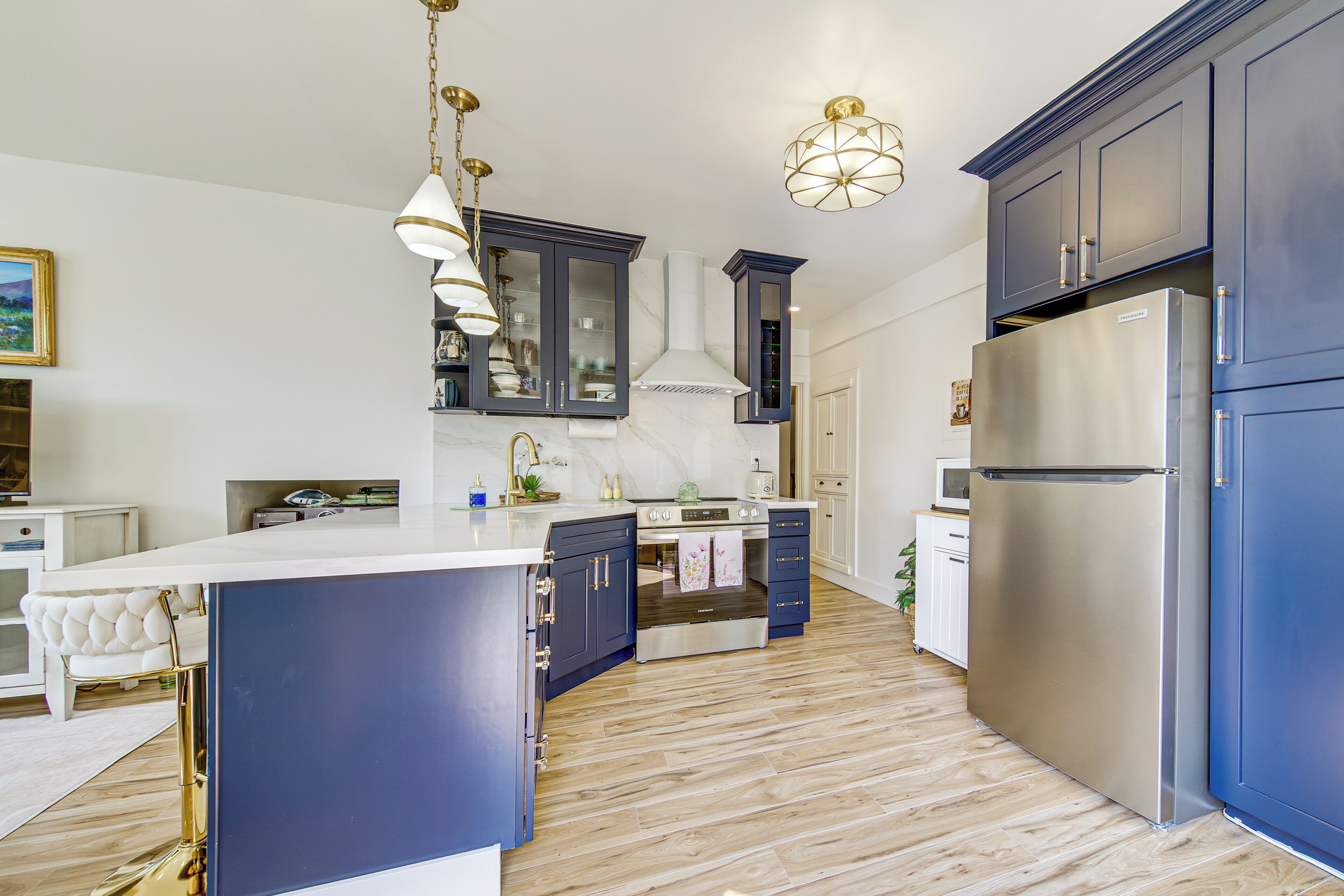 Una cocina moderna con armarios azul oscuro, un refrigerador de acero inoxidable y una encimera de mármol blanco.